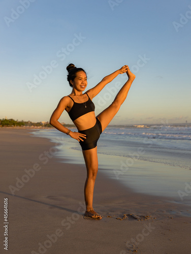 Beach yoga practice. Asian woman practicing one leg up yoga pose. Standing balancing asana. Slim body. Strong legs. Copy space. Fit and healthy. Yoga retreat. Seminyak beach, Bali
