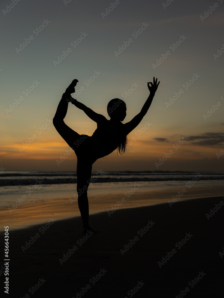 Yoga silhouette. Sunset beach yoga. Slim woman practicing standing asana Natarajasana, Lord of the Dance Pose. Balancing, back bending asana. Copy space. Seminyak beach, Bali