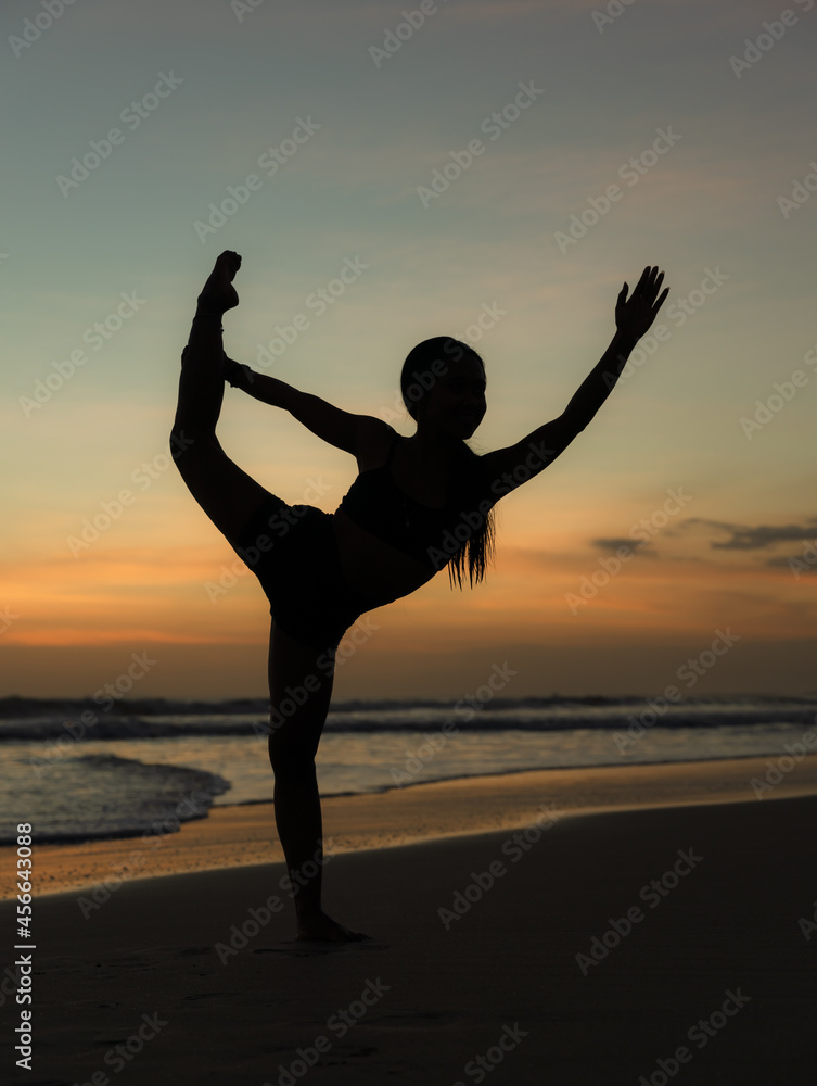 Yoga silhouette. Sunset beach yoga. Slim woman practicing standing asana Natarajasana, Lord of the Dance Pose. Balancing, back bending asana. Exercise on the beach. Seminyak beach, Bali