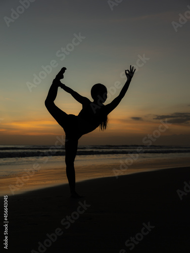 Yoga silhouette. Sunset beach yoga. Slim woman practicing standing asana Natarajasana  Lord of the Dance Pose. Balancing  back bending asana. Copy space. Seminyak beach  Bali