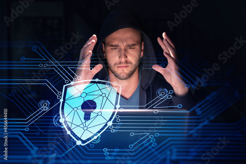 Handsome businessman in hoodie at workplace working with laptop to defend customer cyber security. Concept of clients information protection and brainstorm. Padlock hologram over office background photo