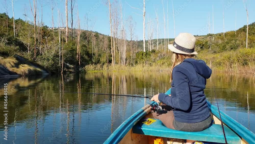 A girl fishing from a canoe on a calm lake next to a beautiful forest A girl fishing from a canoe on a calm lake next to a beautiful forest