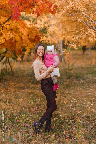 young beautiful mother keeps a one-year-old girl on an autumn natural background
