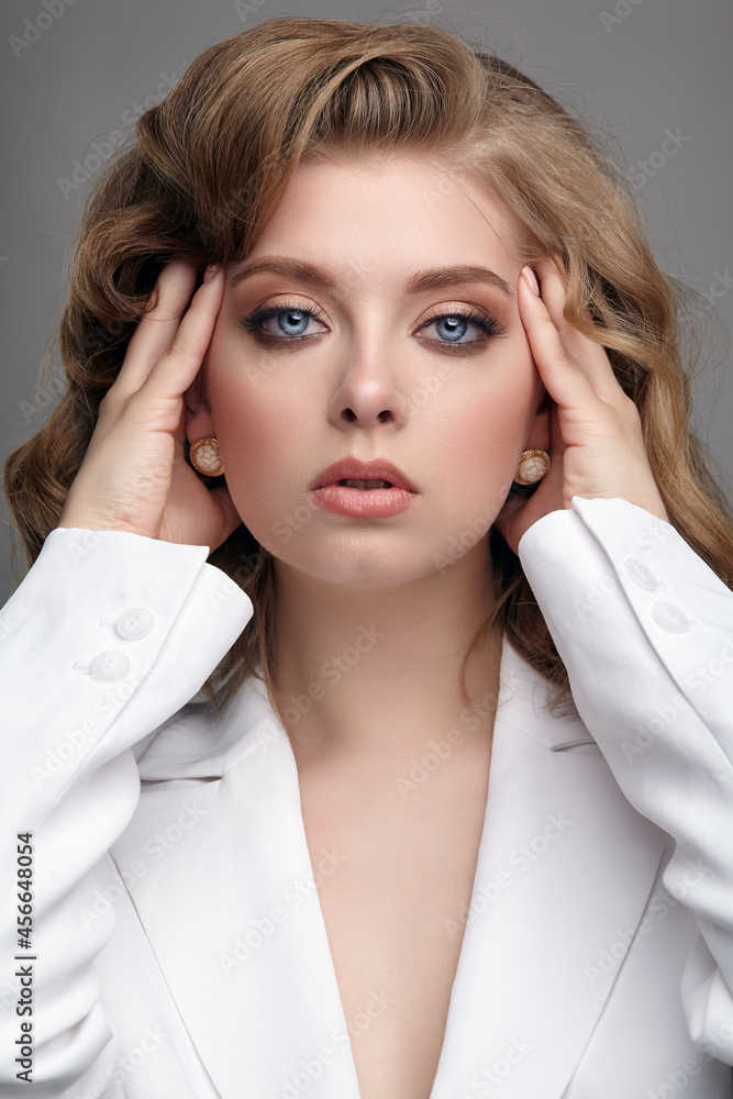 Portrait of young dark blonde woman in casual white jacket with hands near head. Portrait of young dark blonde woman in casual white jacket with hands near head.