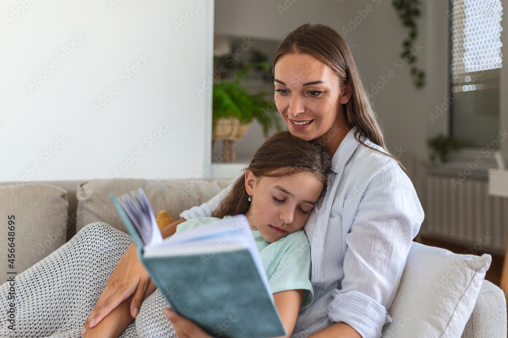 Loving young mother reading book to adorable little daughter, sitting on cozy sofa in living room, mum teaching preschool girl child, family spending weekend at home together, children education Loving young mother reading book to adorable little daughter, sitting on cozy sofa in living room, mum teaching preschool girl child, family spending weekend at home together, children education