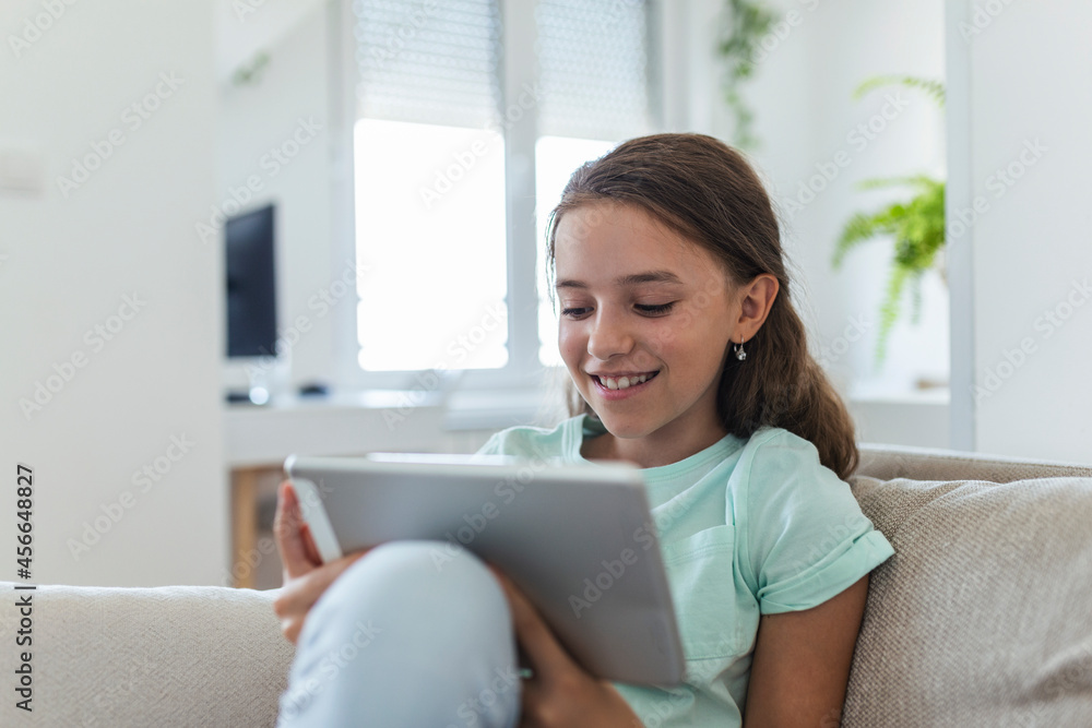 cute little happy girl smile sitting down on sofa using looking digital tablet pad in the living room at home. family activity concept. cute little happy girl smile sitting down on sofa using looking digital tablet pad in the living room at home. family activity concept.