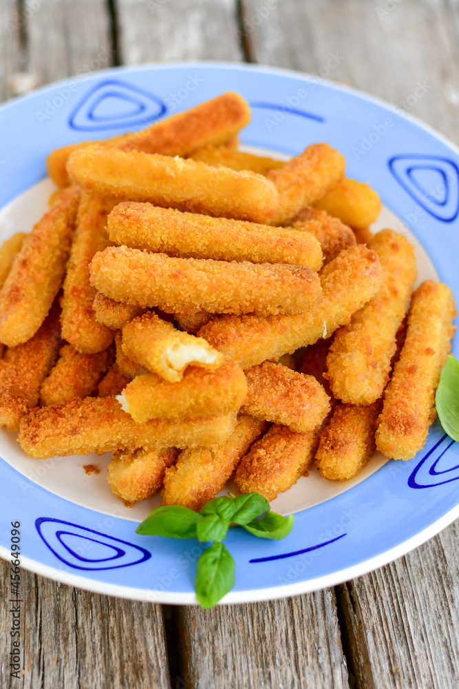 Vegetarian cheese breaded oven baked mozzarella sticks with fresh basil on wooden background Vegetarian cheese breaded oven baked mozzarella sticks with fresh basil on wooden background