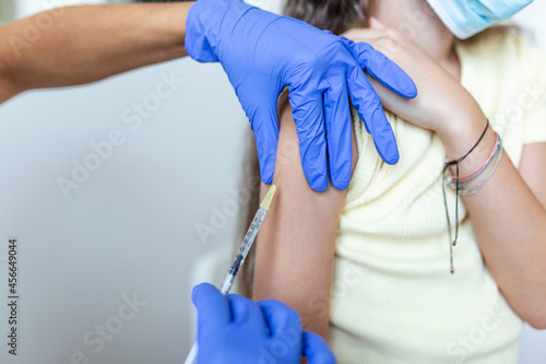 Doctor vaccinating girl. Injecting COVID-19 vaccine into patient s arm. Girl in medical masks getting vaccinated against covid-19  doctor giving injection of coronavirus vaccine at hospital.