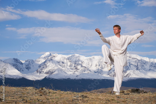 Wushu master in a white sports uniform training kungfu in nature on background of snowy mountains. photo