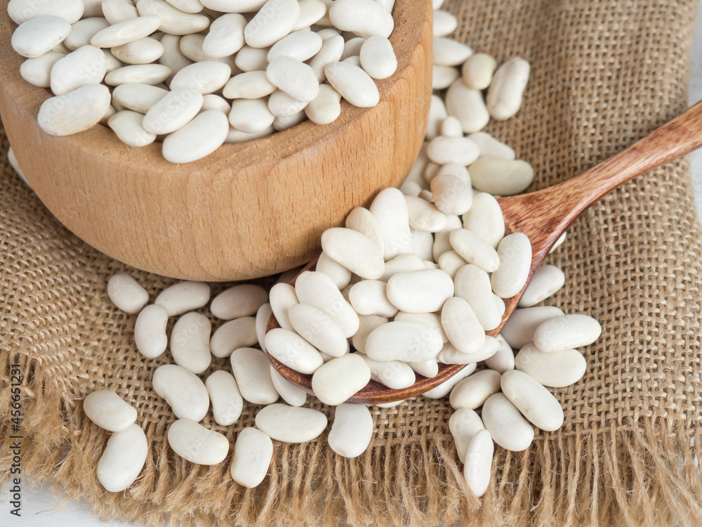 white beans in a wooden spoon on a white wooden table, copy space white beans in a wooden spoon on a white wooden table, copy space