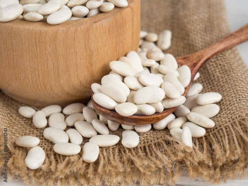 white beans in a wooden spoon on a white wooden table, copy space white beans in a wooden spoon on a white wooden table, copy space