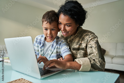 Boy sitting at the knees of his military mother and looking at the laptop screen