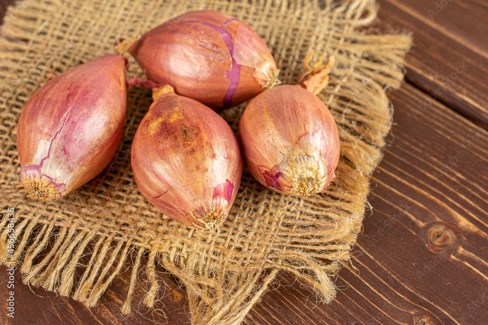 Group of four whole shallot on natural sackcloth on brown wood Group of four whole shallot on natural sackcloth on brown wood
