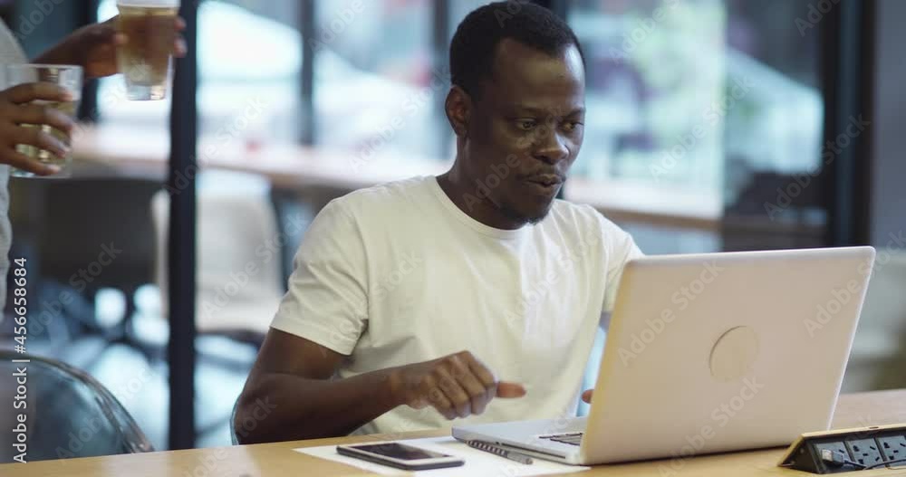 black man working at his laptop with lover's company in the bar.drinking beer and toast with each other black man working at his laptop with lover's company in the bar.drinking beer and toast with each other