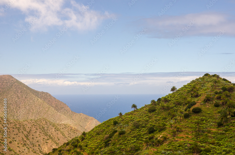 Wide angle shot of beautiful coastline on the Canary island of La Gomera in spring with seashore, mountains, vegetation, sky, clouds and sun; Spain in Europe Wide angle shot of beautiful coastline on the Canary island of La Gomera in spring with seashore, mountains, vegetation, sky, clouds and sun; Spain in Europe