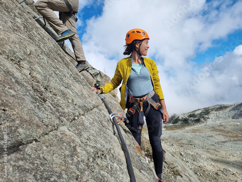 Via Ferrata hiking climbing on the top of Whistler Peak. Guided tour group activity for tourists travel in British Columbia, BC, Canada vacation. Asian woman hiker happy.