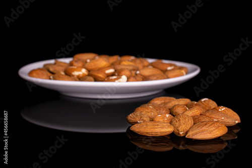 Lot of whole almond in small group aside of the rest on white ceramic plate on black glass