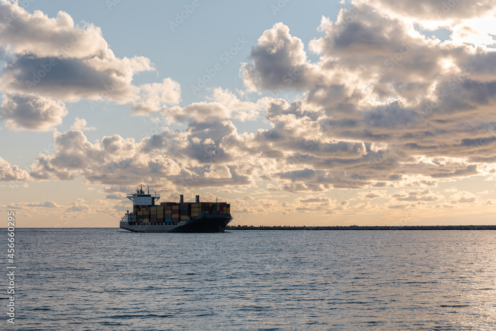 a large commercial cargo ship is entering the port against the backdrop of a sunset sky