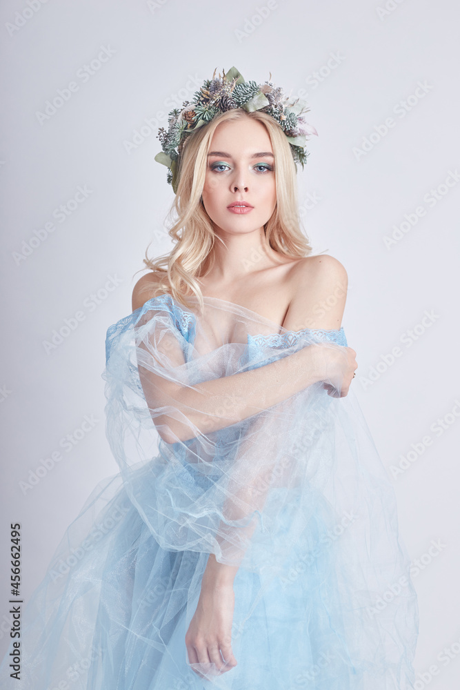 Charming fairy woman in blue ethereal dress and wreath on head on white background, gentle mysterious blonde girl with perfect skin and makeup. Cleanliness, body care and skin Charming fairy woman in blue ethereal dress and wreath on head on white background, gentle mysterious blonde girl with perfect skin and makeup. Cleanliness, body care and skin
