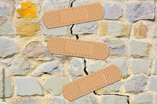 Old cracked and damaged stone wall cause due to subsidence of foundations structural failures - concept with adhesive bandage photo