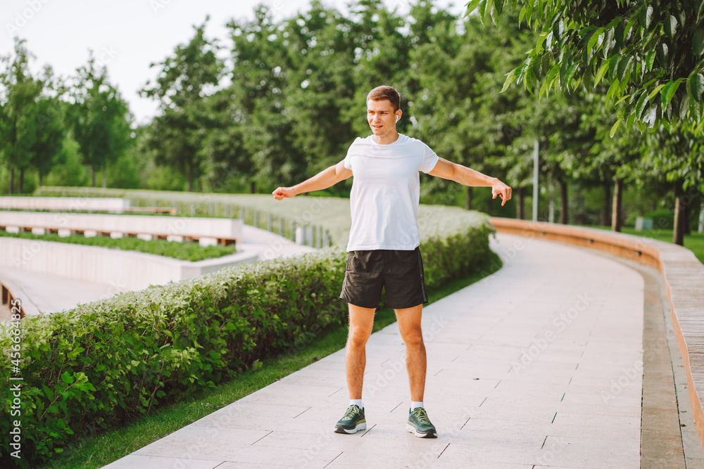 Attractive man athlete wearing sportswear do stretching exercises in modern park at summer morning