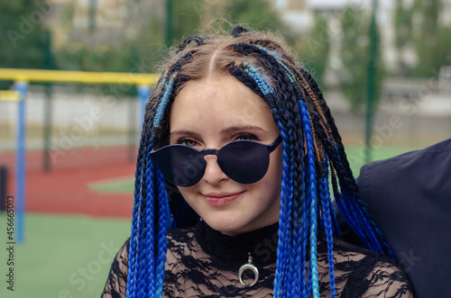 Portrait of a young woman with blue pigtails. Woman wearing blue sunglasses looking at the camera. Summer, daytime.