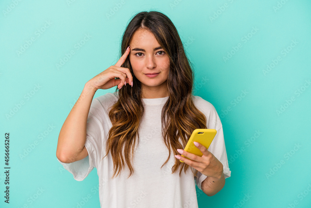 Young caucasian woman holding a mobile phone isolated on blue background pointing temple with finger, thinking, focused on a task. Young caucasian woman holding a mobile phone isolated on blue background pointing temple with finger, thinking, focused on a task.