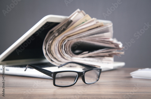 Newspapers, computer, eyeglasses on the wooden table.