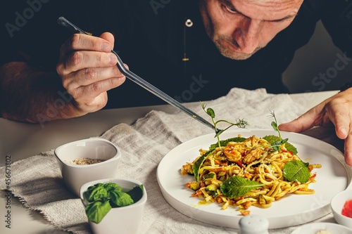 The chef prepares traditional seafood pasta marinara. The chef decorates the dish with herbs using tweezers. Spaghetti with seafood. Restaurant serving dish. People working. Catering business