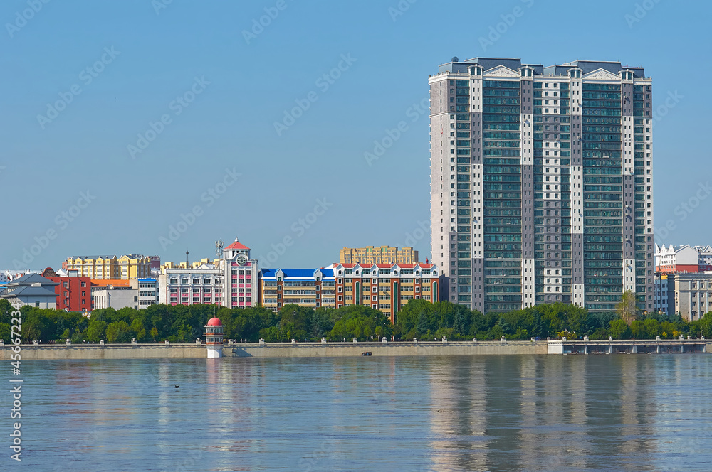 Sunny view of the embankment of the city of Heihe, China from the city of Blagoveshchensk, Heihe. Reflections of buildings in the Amur river. The period of danger of flooding.