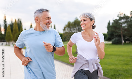 Happy senior husband and wife in sportive outfits running outdoors in city park