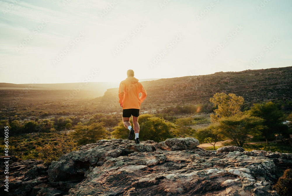 Caucasian male athlete having a break from outdoor run hiking reaching mountain peak watching beautiful sunset