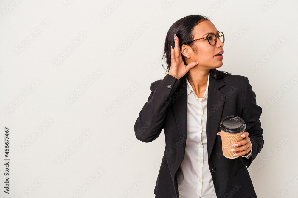 Young business latin woman holding a take away coffee isolated on white background trying to listening a gossip. Young business latin woman holding a take away coffee isolated on white background trying to listening a gossip.