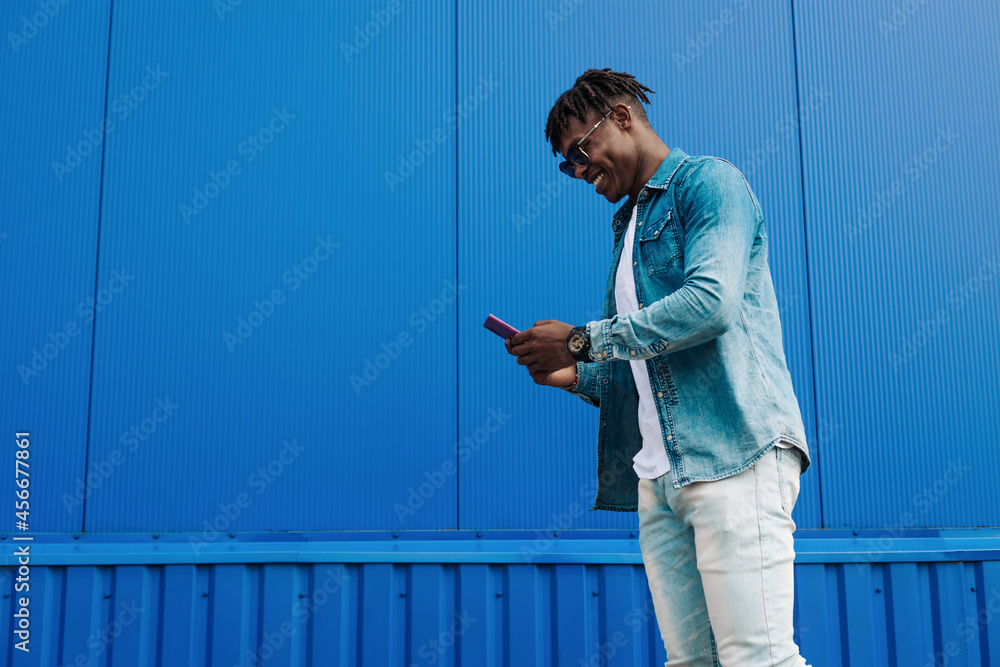 an african guy walks with a phone around the city, against the background of a blue building, makes a purchase online an african guy walks with a phone around the city, against the background of a blue building, makes a purchase online