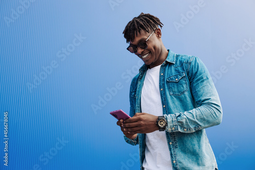 african man in sunglasses typing sms over blue background, 5g internet concept, high speed internet on phone
