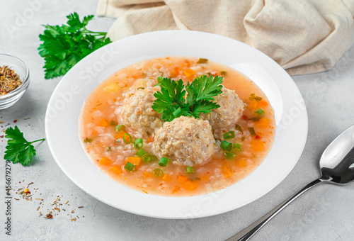 Healthy soup with turkey meat meatballs with vegetables in a white plate on a gray background.