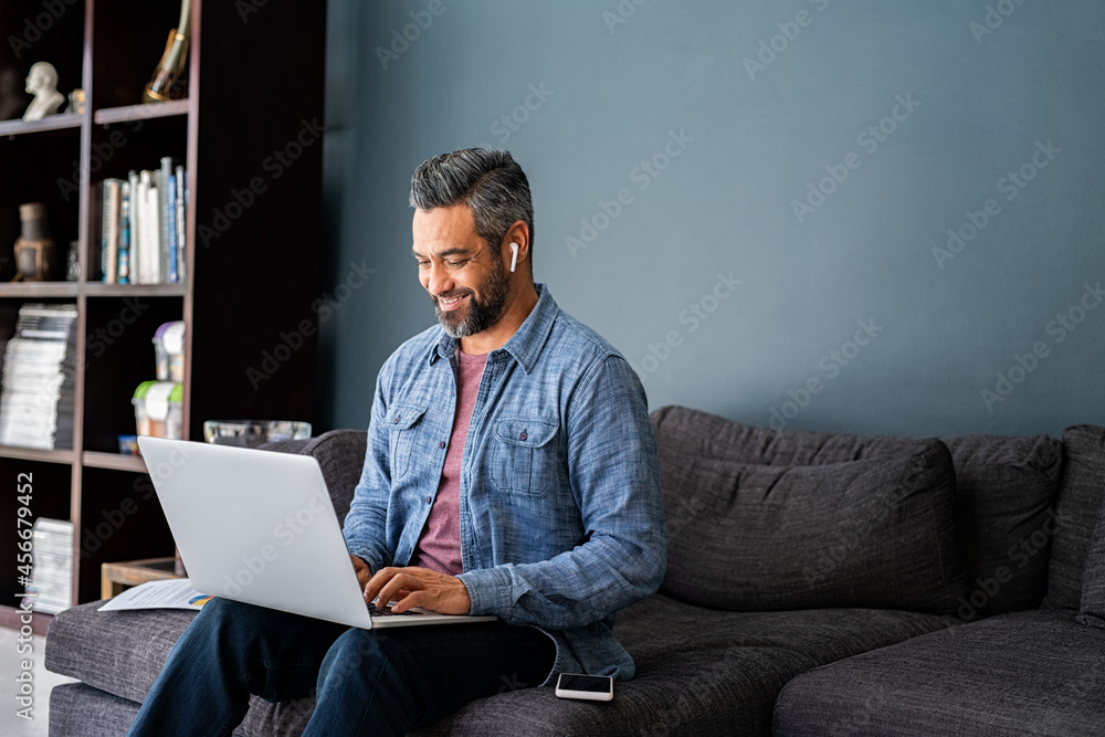 Indian man typing on laptop while working from home - obrazy, fototapety, plakaty 