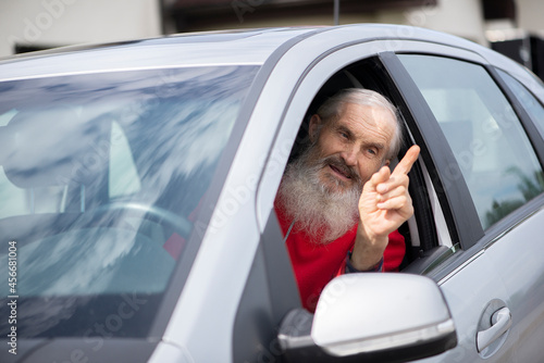 Senior man driver in car. Emotional portrait of an expressive and impulsive senior caucasian male driver with lond beard, showing  his finger in air and shouting to the oncoming car driver. photo