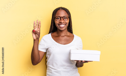 smiling and looking friendly, showing number three or third with hand forward, counting down and holding an empty box photo