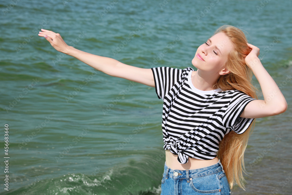 Beautiful young woman near sea on sunny day in summer