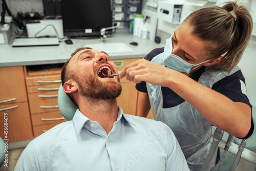 Caucasian female dentist cleaning teeth of male client sitting in dentist chair 