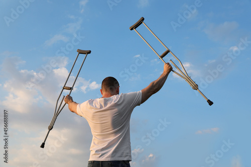 Fotografi Man raising hands with underarm crutches up to sky outdoors, back view