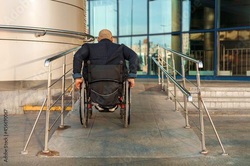 Man wearing jacket riding in wheelchair on ramp by building photo