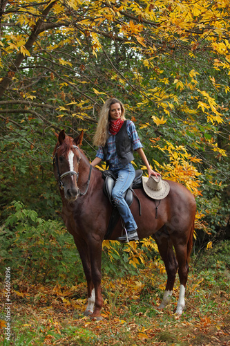 Beautiful cowgirl ride her horse in autumn country road at sunset