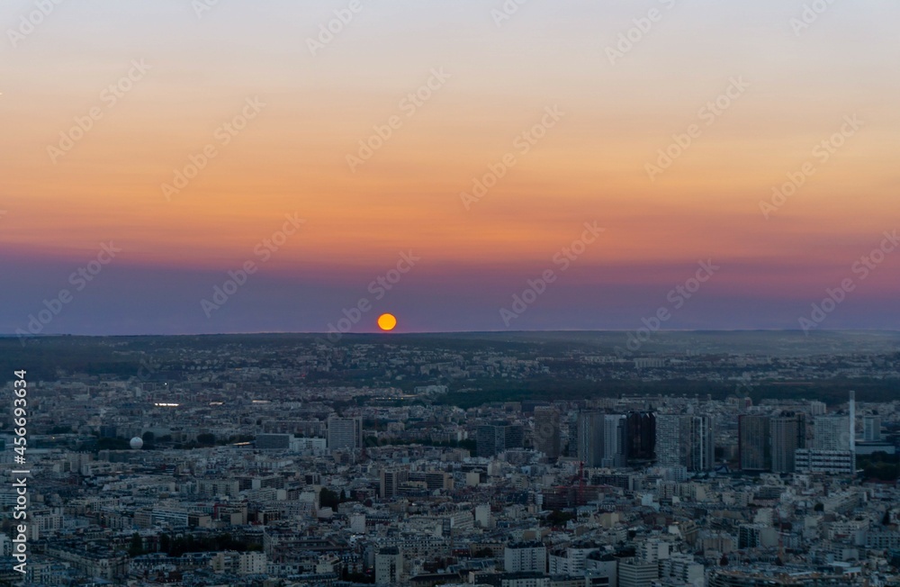 The orange sun disappearing into the dimly lit city skyline, with the multi-colored sunset sky