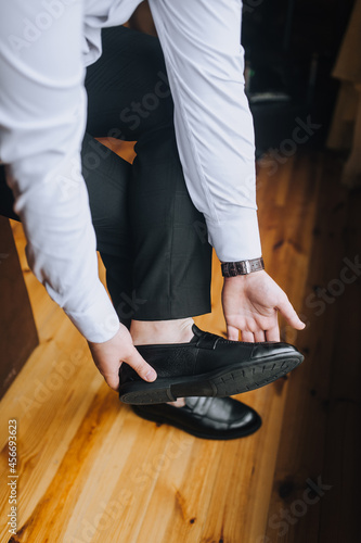 A man businessman in a white shirt puts on black shiny shoes  going to work in the morning.