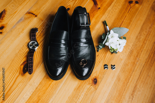 Wedding accessories and details of the groom on a wooden parquet background: black shoes, boutonniere, wristwatch,cufflinks.