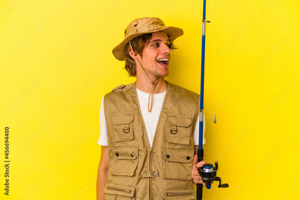 Young fisherman with makeup holding rod isolated on yellow background looks aside smiling, cheerful and pleasant. Young fisherman with makeup holding rod isolated on yellow background looks aside smiling, cheerful and pleasant.