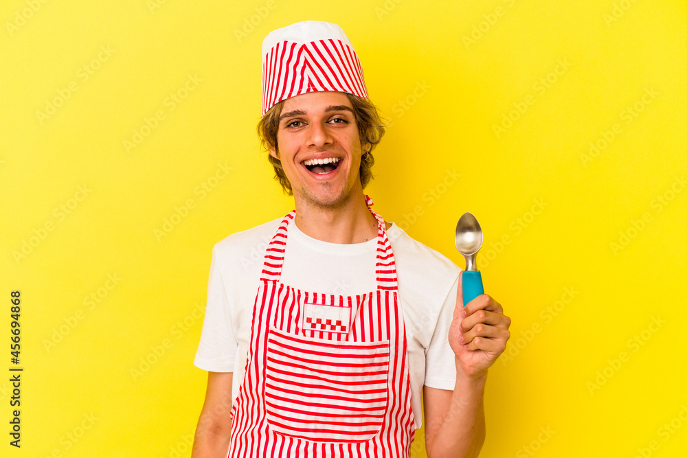 Young ice cream maker man with makeup holding spoon isolated on yellow background happy, smiling and cheerful. Young ice cream maker man with makeup holding spoon isolated on yellow background happy, smiling and cheerful.