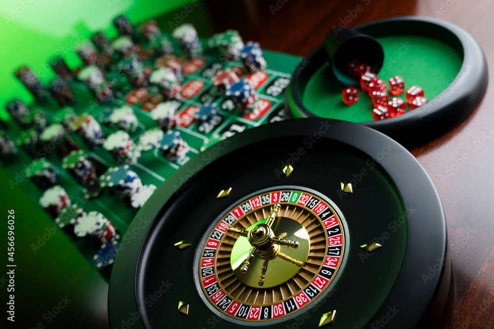 Casino. Gambling games theme. Roulette wheel, dice and poker chips on the casino felt green table.
Casino. Gambling games theme. Roulette wheel, dice and poker chips on the casino felt green table.